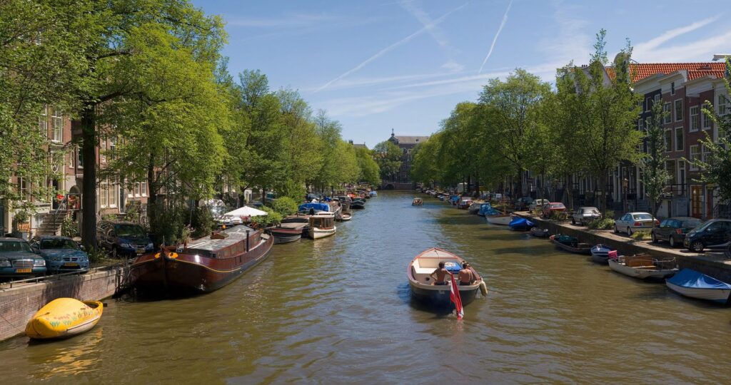 Gracht in der Amsterdamer Innenstadt mit Booten, Giebelhäusern und Baumreihen im Sommer