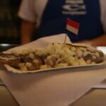 Haring Happen: Ein Führer zum Genuss niederländischer Matjes Matjeshering mit gehackten Zwiebeln und Fähnchen an einem Fischstand in Amsterdam