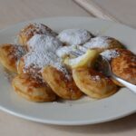 Poffertjes und Pannekoeken: Ein Duell der Pfannkuchen Frisch gebackene Poffertjes mit Butter und Puderzucker auf einem Teller