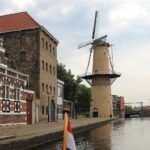 Die Geschichte des Jenever: Hollands Nationalgetränk verstehen Windmühle und historische Speicherhäuser an der Gracht in Schiedam, der Jenever-Stadt