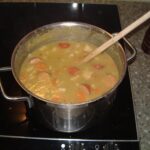 Holländische Erbsensuppe (Erwtensoep): Traditionelles Rezept & Variationen Topf mit dicker Erwtensoep mit Rookworst, Möhren und Kochlöffel auf dem Herd