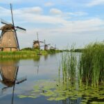 Holland oder Niederlande: Was ist der Unterschied? Windmühlen von Kinderdijk spiegeln sich im Wasser des Poldergrabens