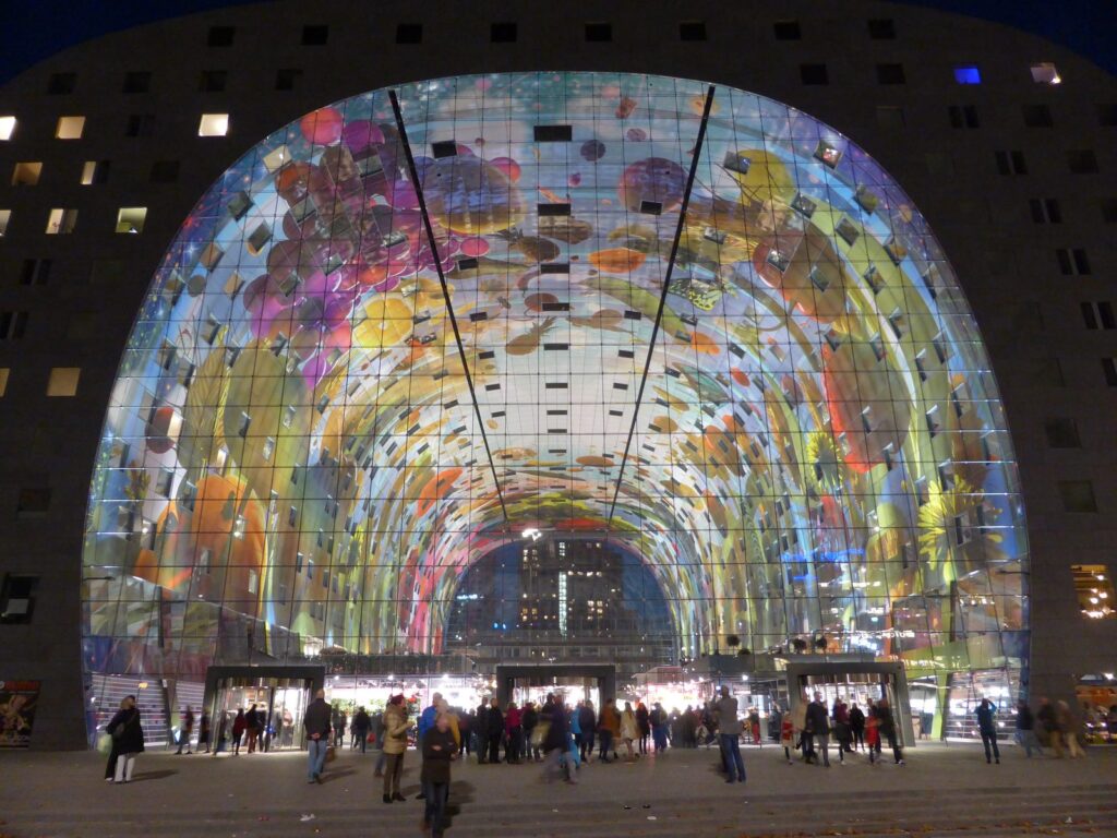 Beleuchteter Torbogen der Markthal in Rotterdam mit Deckengemälde am Abend