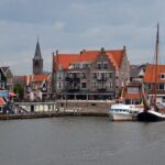Volendam und Marken an einem Tag: Boot, Parken, Museen Hafen von Volendam mit Segelschiffen, Häuserzeile am Deich und Kirchturm